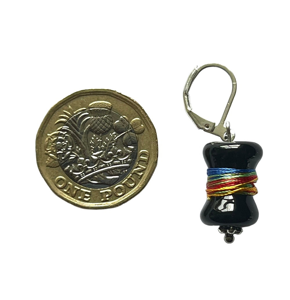 Black bobbin glass bead wrapped with multicolour thread handing from a latch back hook to create a stitch marker. Shown with a pound coin for scale.