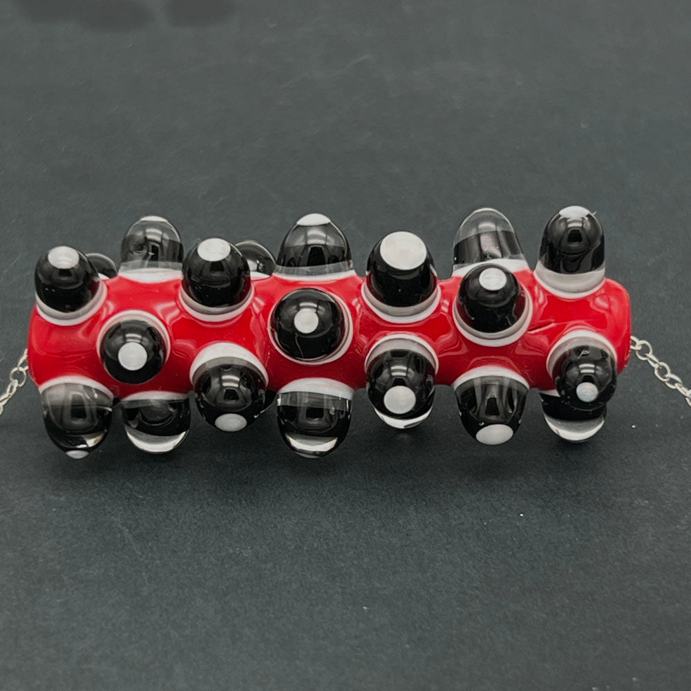 Close up of red, black and white glass bead necklace photographed on a dark background.