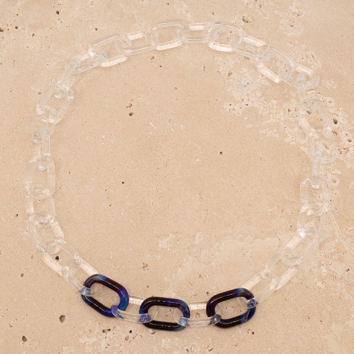 Overhead view, sandstone background, clear glass necklace with three blue links