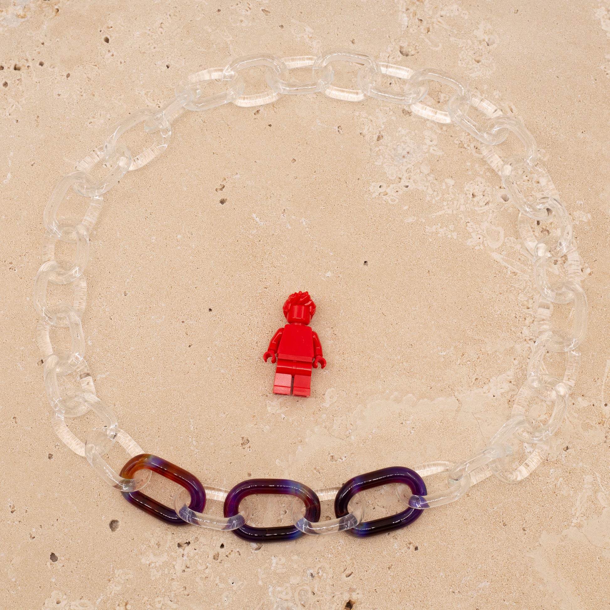 Overhead view of necklace made from clear glass links with 3 coloured links. Image includes a Lego figure for scale.