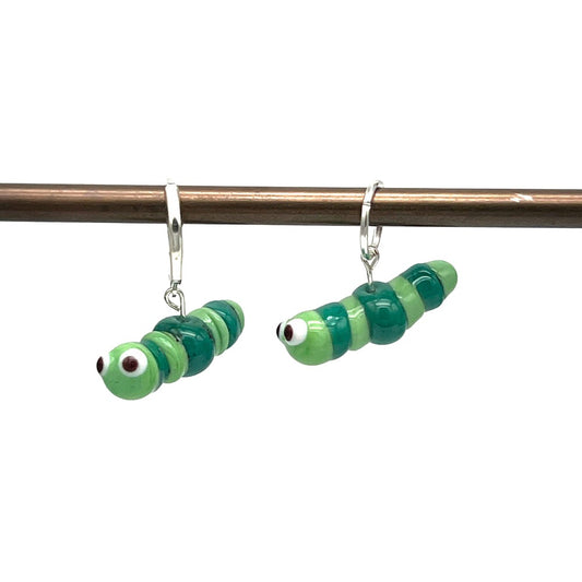 Handcrafted glass caterpillar stitch markers in green and teal, hanging from a metal rod with silver latch back hooks and  jump rings