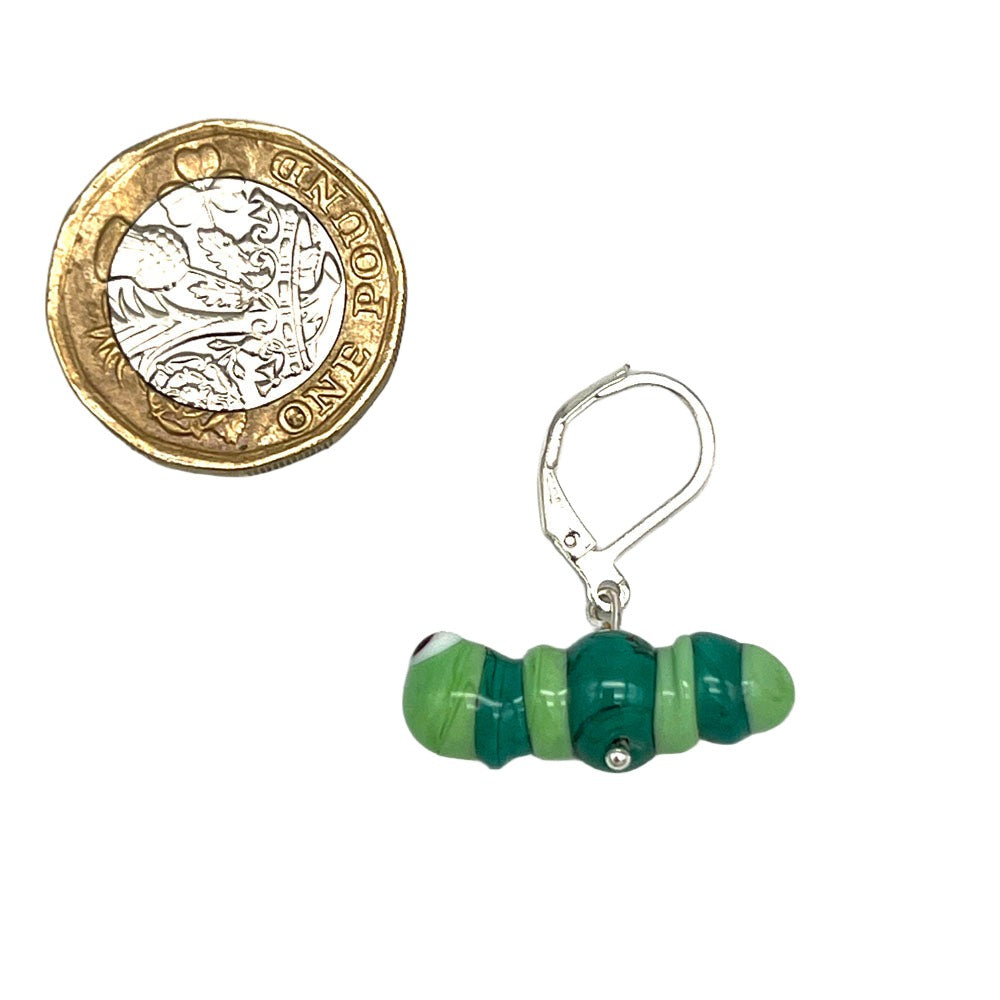Close-up of a green and teal glass caterpillar stitch marker with a silver latch-back hook next to a one-pound coin for size comparison.
