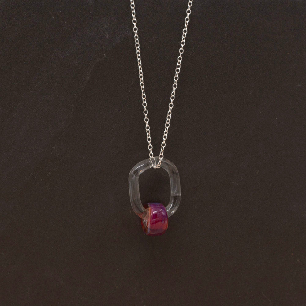 Dark background, a necklace made with a clear link and pink barrel bead.