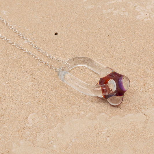 Sandstone tile and a necklace made with a clear glass link which passes through a pink bead.