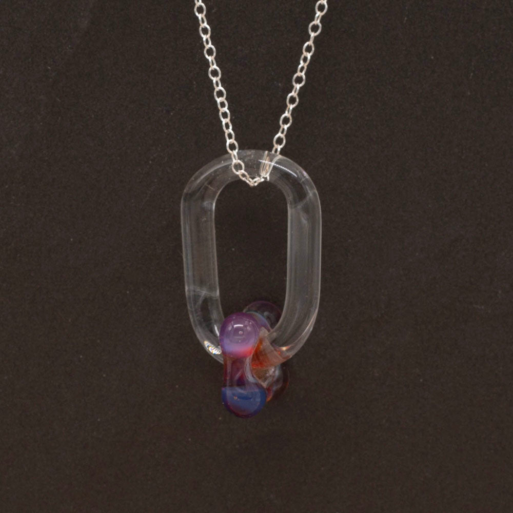 Close up of a necklace made with a clear glass link which passes through a pink bead. Dark background.