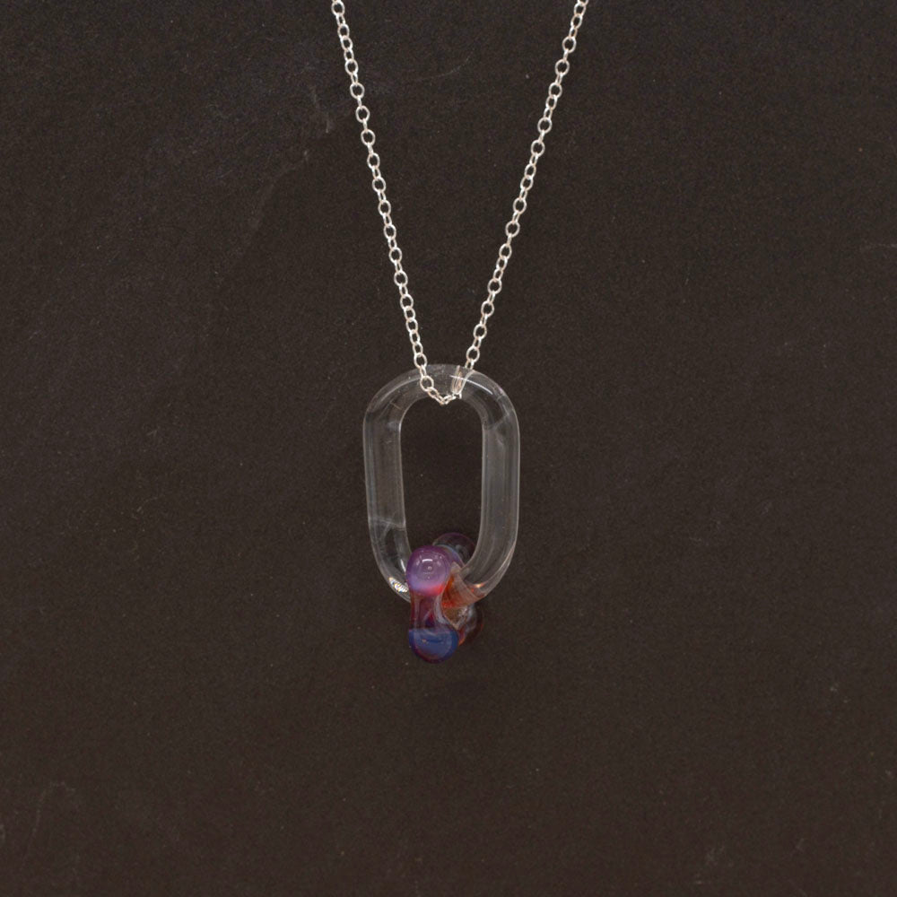 Close up of a necklace made with a clear glass link which passes through a pink bead. Dark background.