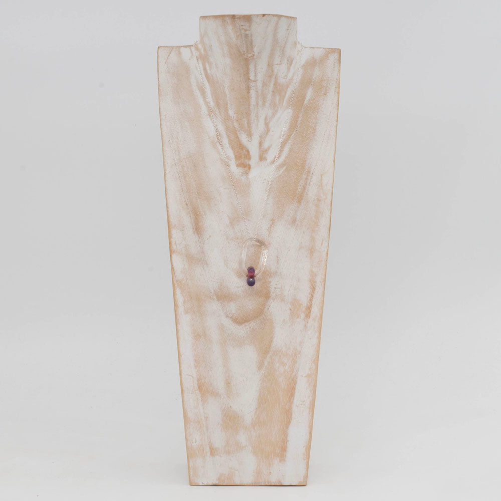 Whitewashed wood bust displaying a necklace made with a clear glass link which passes through a pink bead.