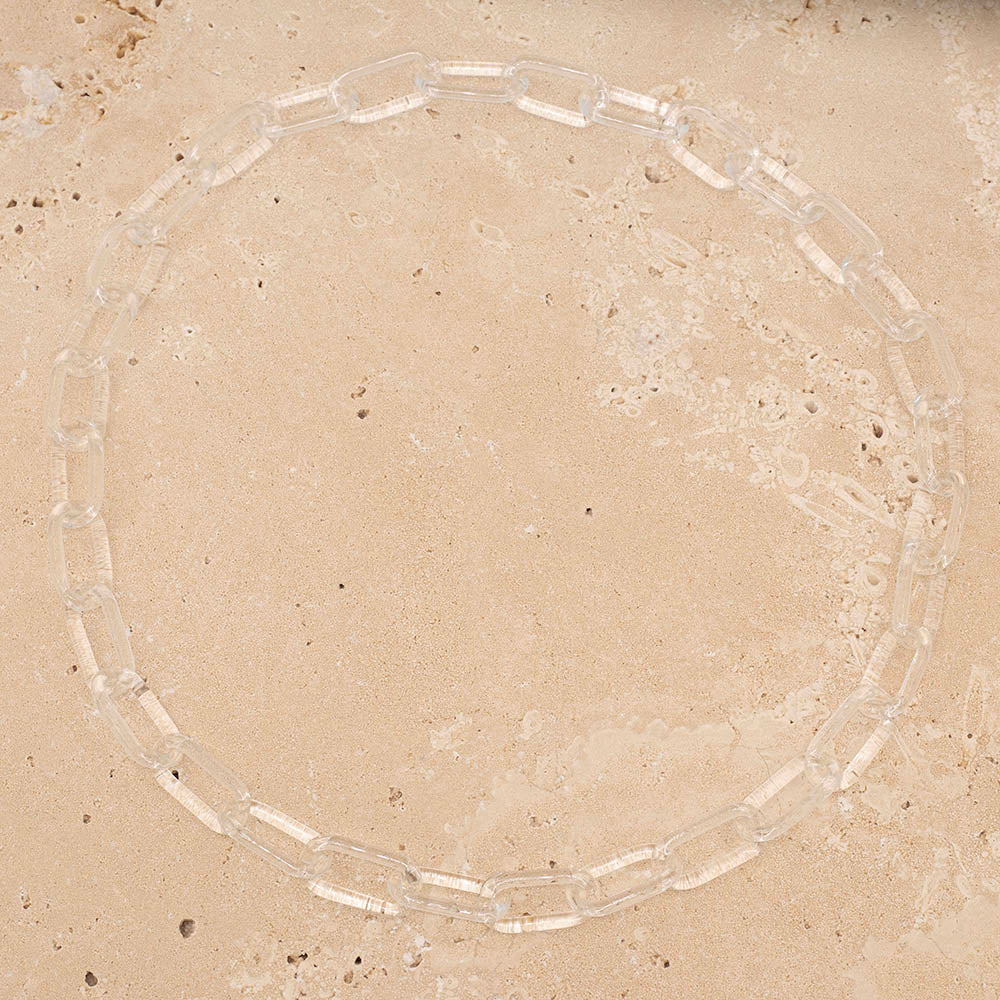 Clear glass chain link necklace photographed from above on sandstone tile.