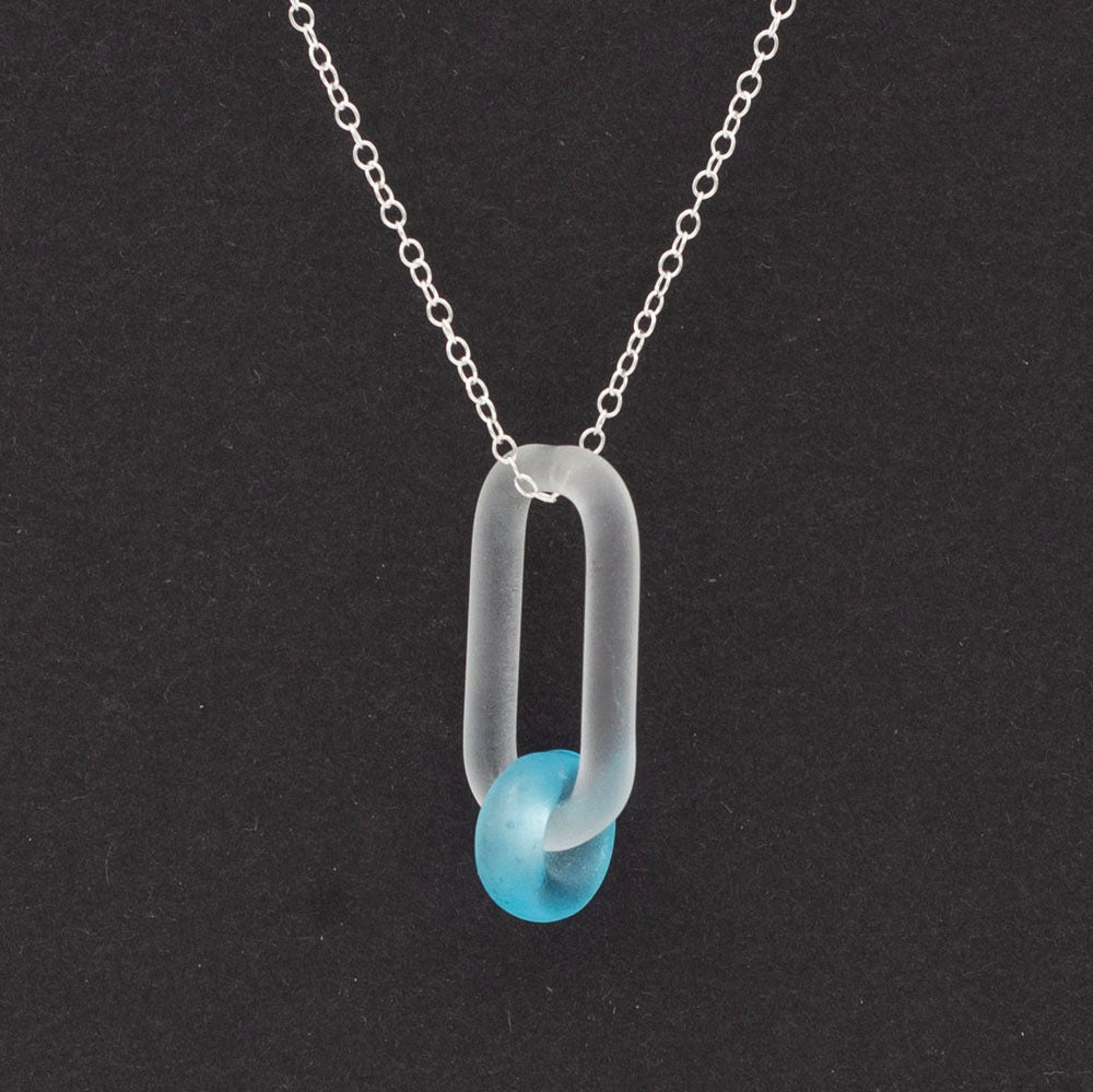 Close up of a necklace with link and Bombay Sapphire gin bottle bead, dark background.