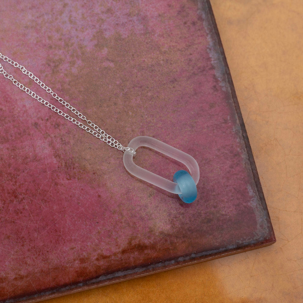 Necklace with link and Bombay Sapphire gin bottle bead, photographed on pink and yellow tiles.