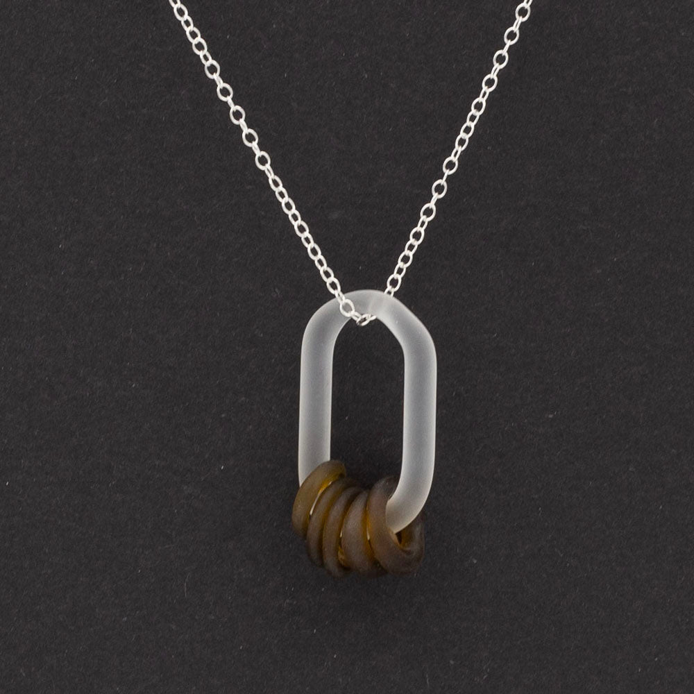 Close up of a frosted link made from clear glass which passes through five beads. Dark background.