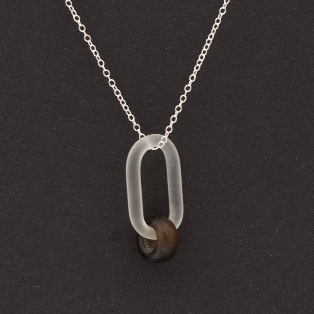 Close up of frosted clear glass link and marmite glass bead necklace photographed on dark background.