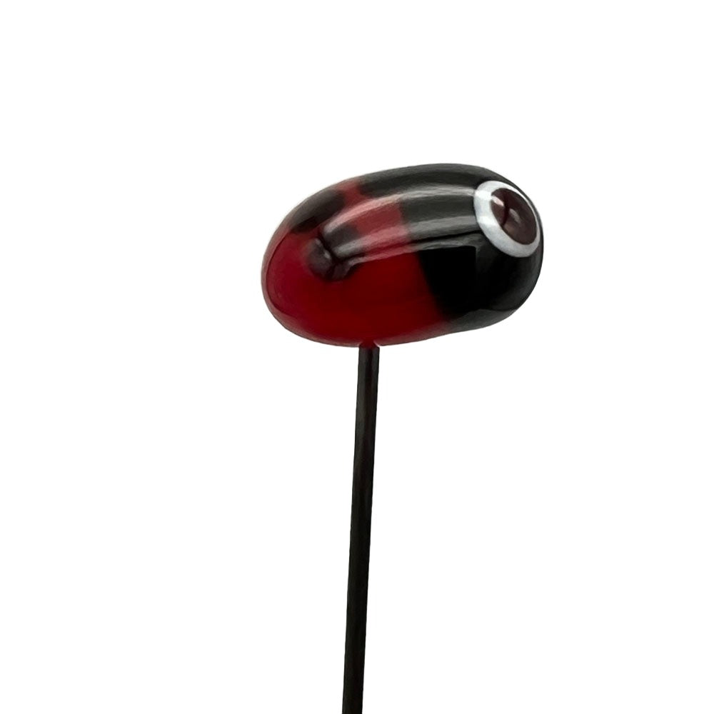 Handmade glass ladybird pin with a red body and black head, side view, on a stainless steel pin