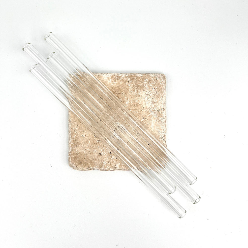 Four long clear glass straws sit across a small sandstone tile. Photograph taken from above.