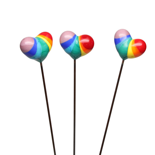 Three handmade rainbow glass heart plant decorations lined up on a white background, showing how each one varies slightly in colour placement and shape