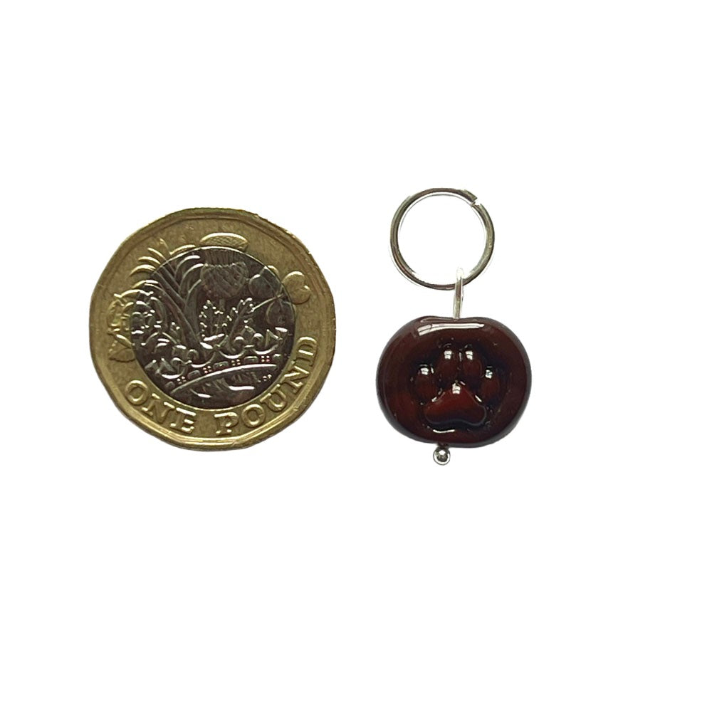 Brown bead with paw print imprint  on a jump ring stitch marker shown with a pound coin for scale