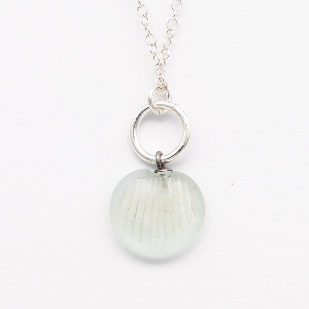 Close up of pale blue frosted glass charm with shell imprint on a plain white background. The charm is frosted, and spiral is shiny. The charm hangs on a large silver jump ring. The necklace is completed with a small silver jump ring and silver chain.