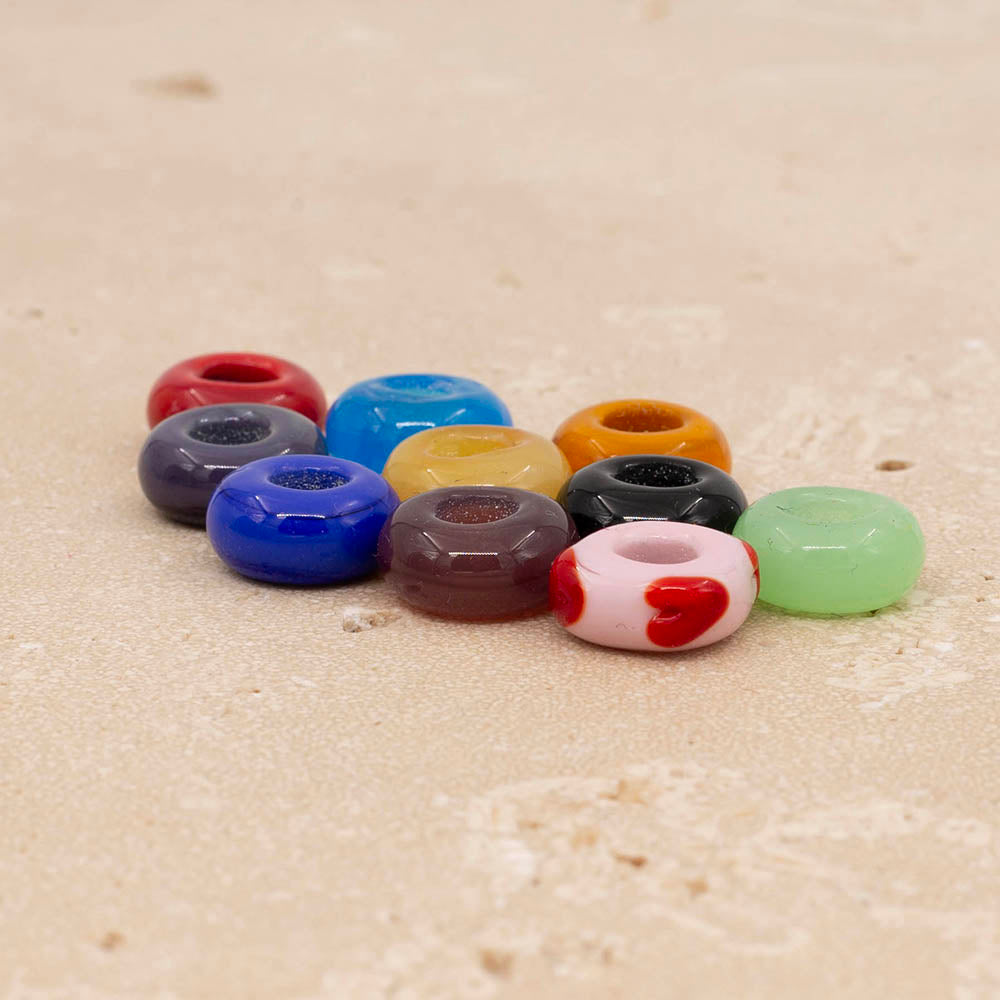 Ten big hole glass beads in red, purple. turquoise, blue, yellow, gold, plum, black, pale green and pale pink with red hearts. The beads sit on a sandstone tile.