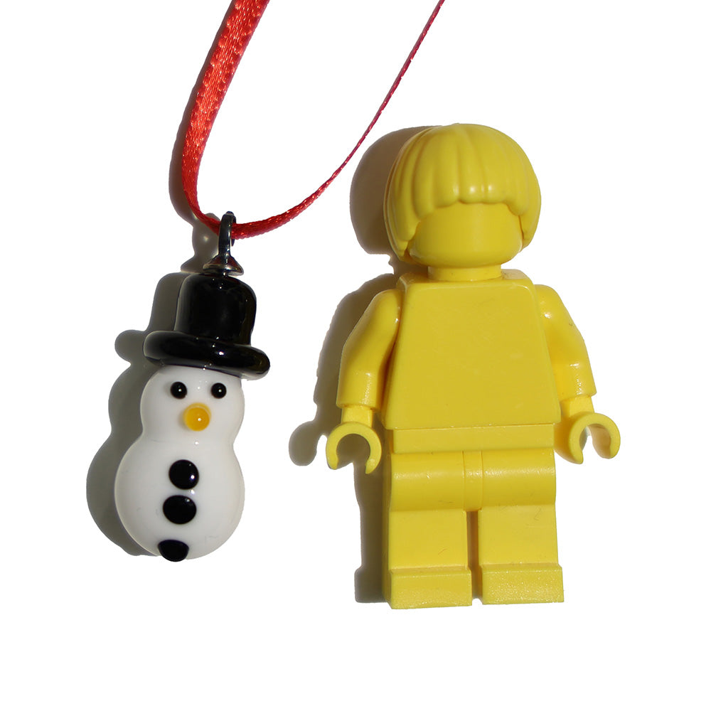 Glass snowman decoartion with black hat, coal eyes and carrot nose, shown with a lego figure for scale.