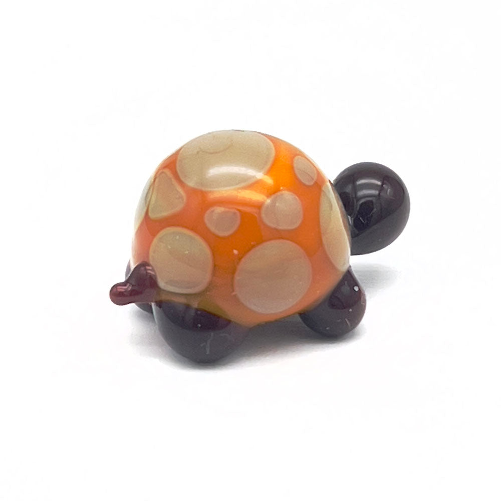 A yellow and grey glass tortoise with light grey spots on its shell, viewed from the back.