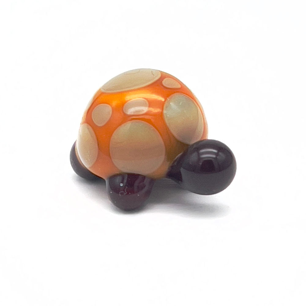 A yellow and grey glass tortoise with light grey spots on its shell, viewed from the front.