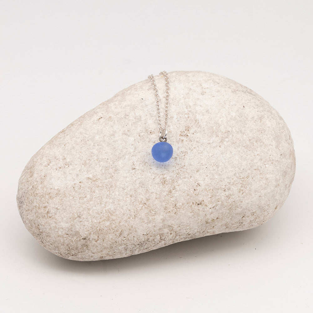 blue glass ball charm necklace on a pale grey rock