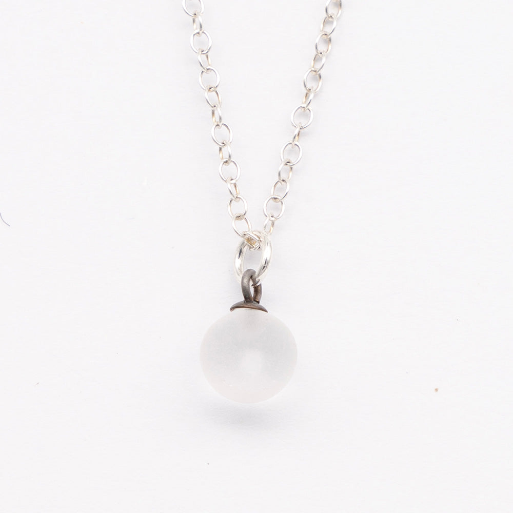 Close up of a clear frosted glass ball charm on a plain white background. The charm is frosted. It hangs on a small silver jump ring. The necklace is completed with a silver chain.