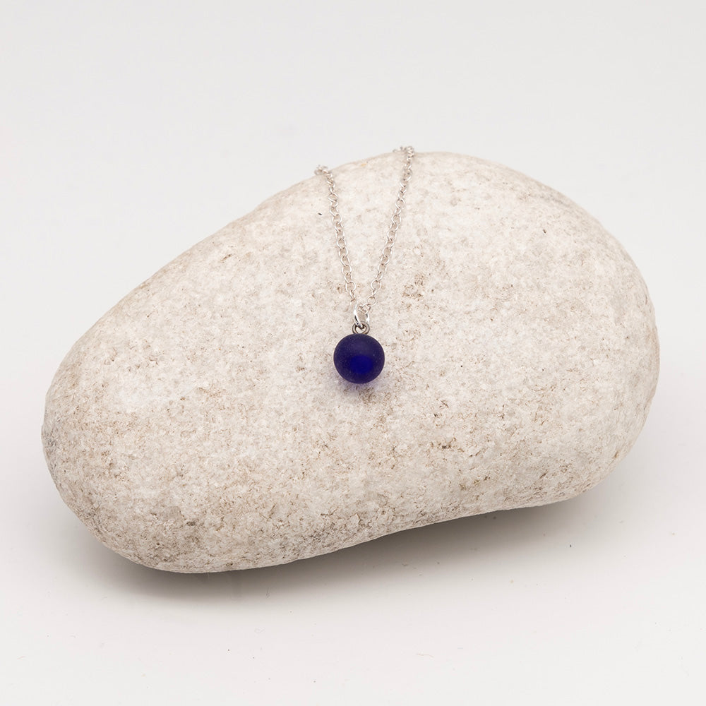 dark blue glass ball charm necklace on a pale grey rock