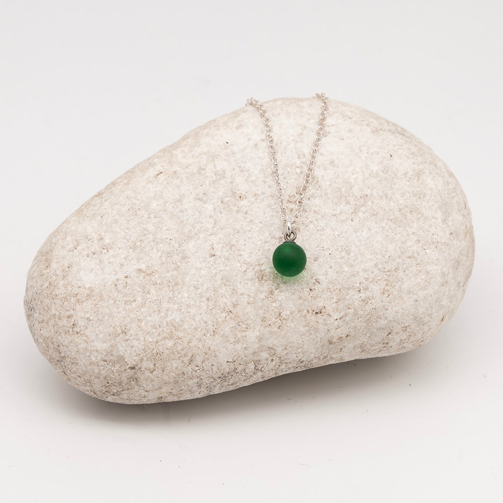 green glass ball charm necklace on a pale grey rock