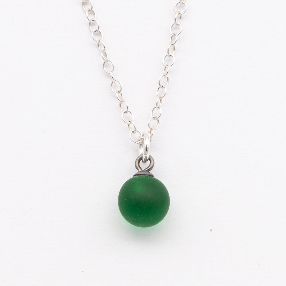 Close up of a green frosted glass ball charm on a plain white background. The charm is frosted. It hangs on a small silver jump ring. The necklace is completed with a silver chain.