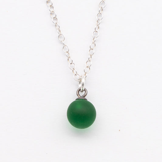 Close up of a green frosted glass ball charm on a plain white background. The charm is frosted. It hangs on a small silver jump ring. The necklace is completed with a silver chain.