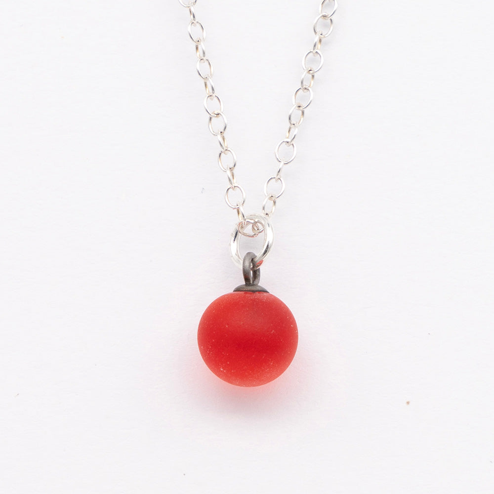 Close up of a orange frosted glass ball charm on a plain white background. The charm is frosted. It hangs on a small silver jump ring. The necklace is completed with a silver chain.