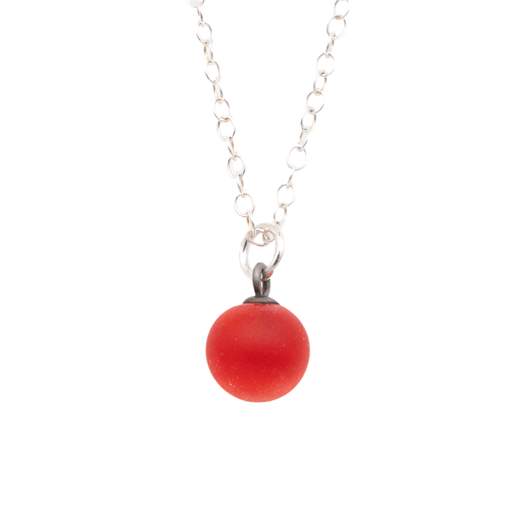 Close up of a orange frosted glass ball charm on a plain white background. The charm is frosted. It hangs on a small silver jump ring. The necklace is completed with a silver chain.