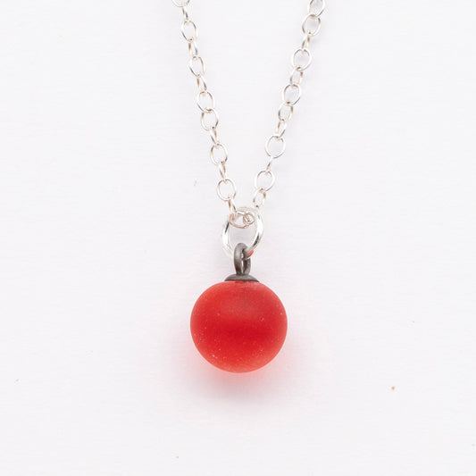 Close up of a orange frosted glass ball charm on a plain white background. The charm is frosted. It hangs on a small silver jump ring. The necklace is completed with a silver chain.