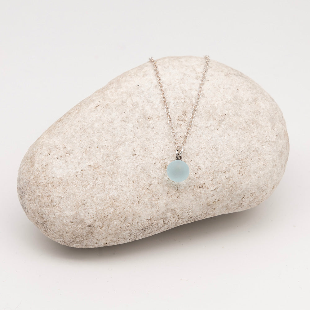 pale blue glass ball charm necklace on a pale grey rock