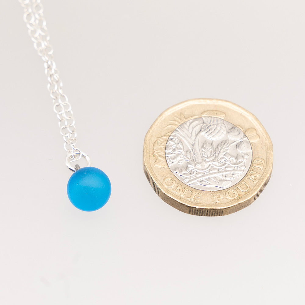 Glass ball necklace shown with pound coin for scale. The glass charm is roughly quarter of the size of the coin.