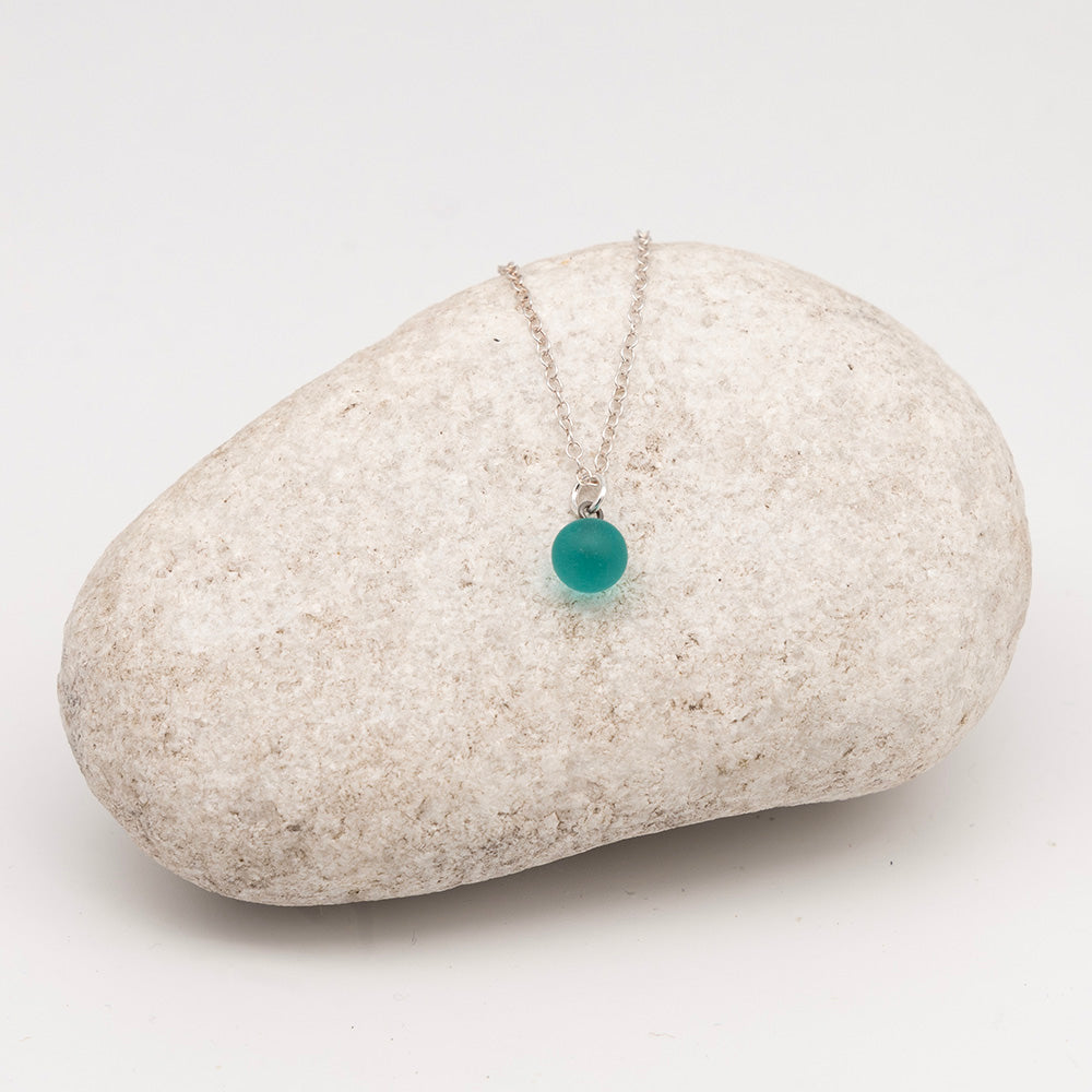 teal glass ball charm necklace on a pale grey rock