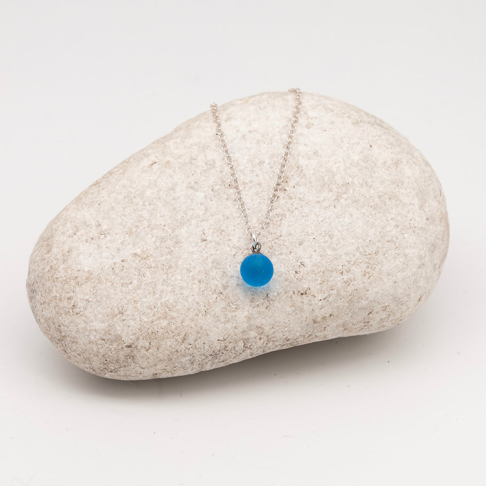 turquoise glass ball charm necklace on a pale grey rock