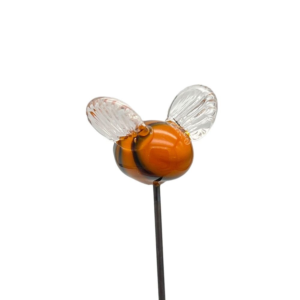 Close-up view of a handmade lampwork glass bee plant decoration, showing its yellow and black striped body with clear glass wings, against a plain background.