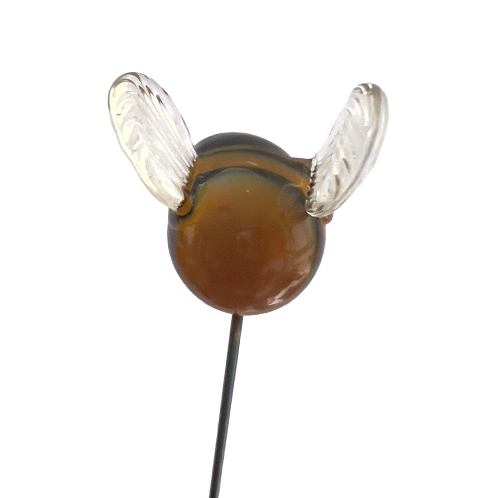 A close-up of a glass bee plant decoration viewed from the back. The bee has translucent wings and a rounded, amber-colored body mounted on a thin metal stake.