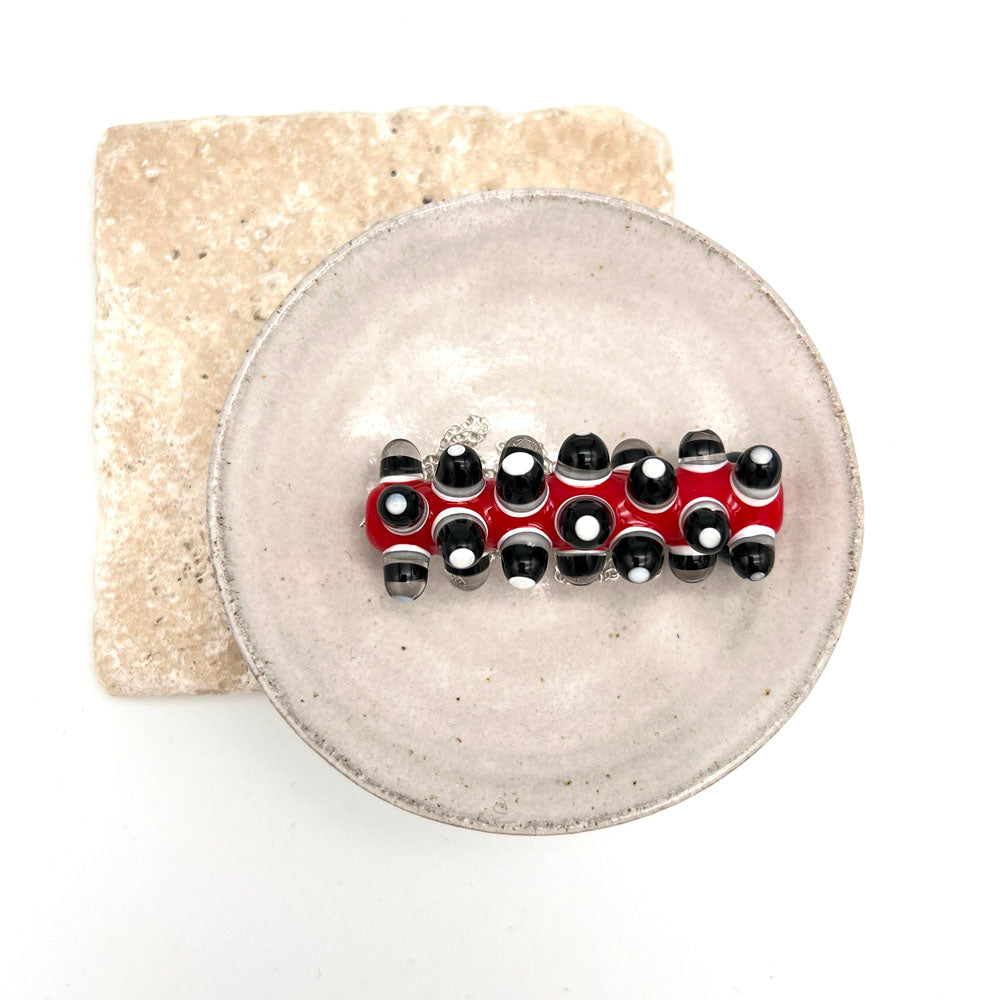 Red glass bad necklace with black and white dots in a small white ceramic bowl. Photographed from above.