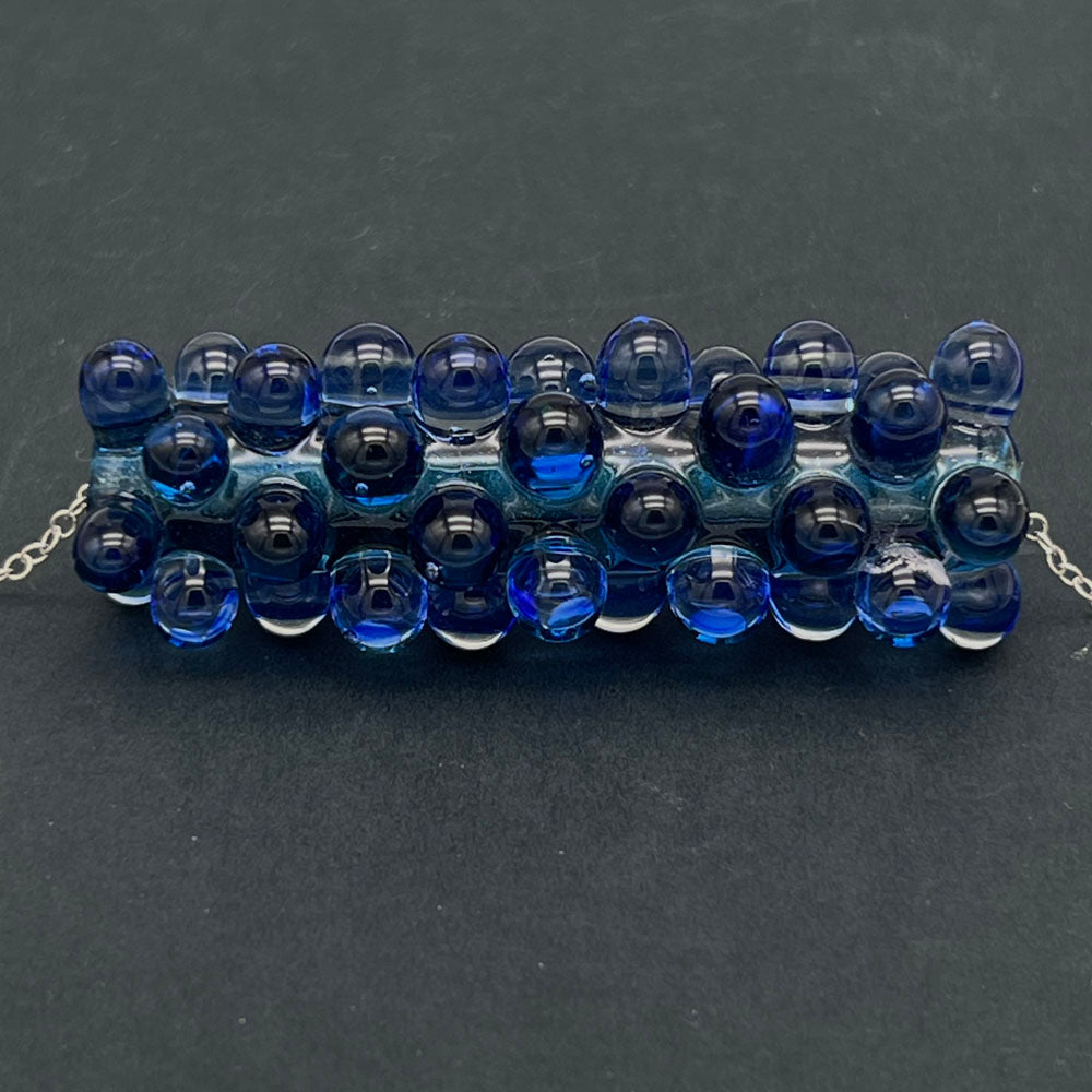 Close up of blue ripples bead necklace shown on a dark background