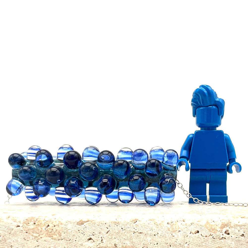 Blue ripples necklace shown beside a blue Lego figure for scale. The width of the bead comes up to the elbow of the figure.