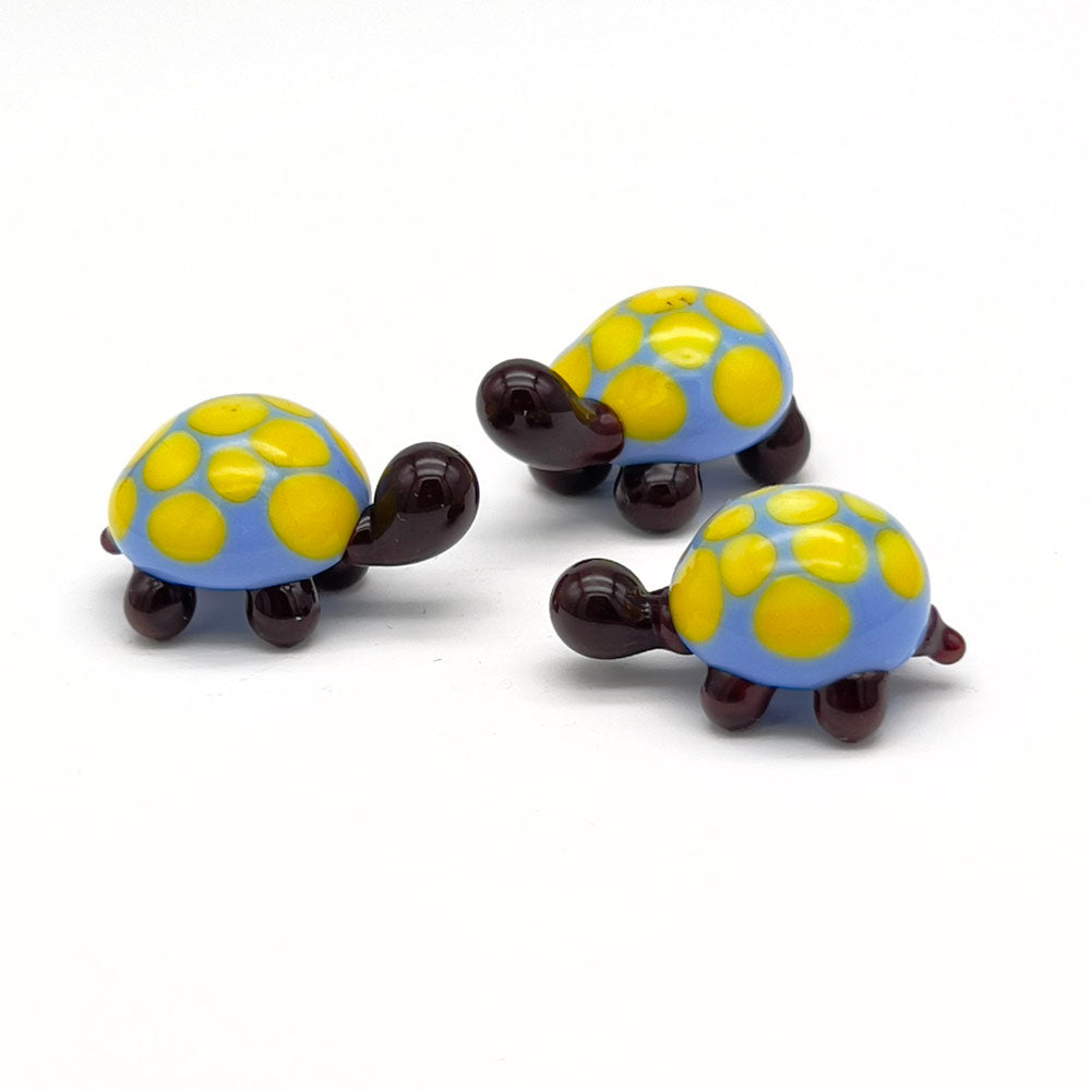 A group of three similar glass tortoises, each with a blue shell and yellow spots, dark brown heads, and legs, arranged on a white background.