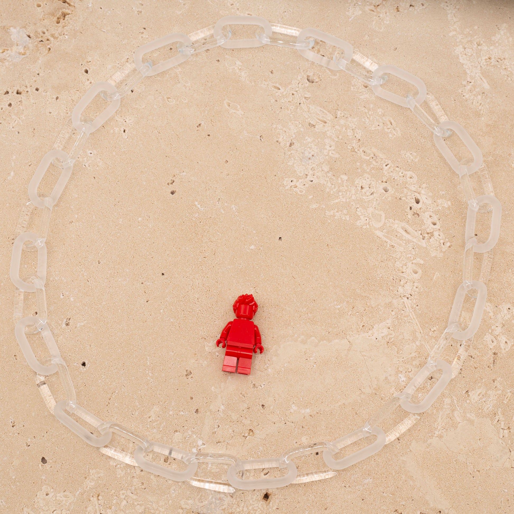 Overhead view, glass necklace made with bold links of alternating clear and frosted glass. Image includes Lego figure for scale.