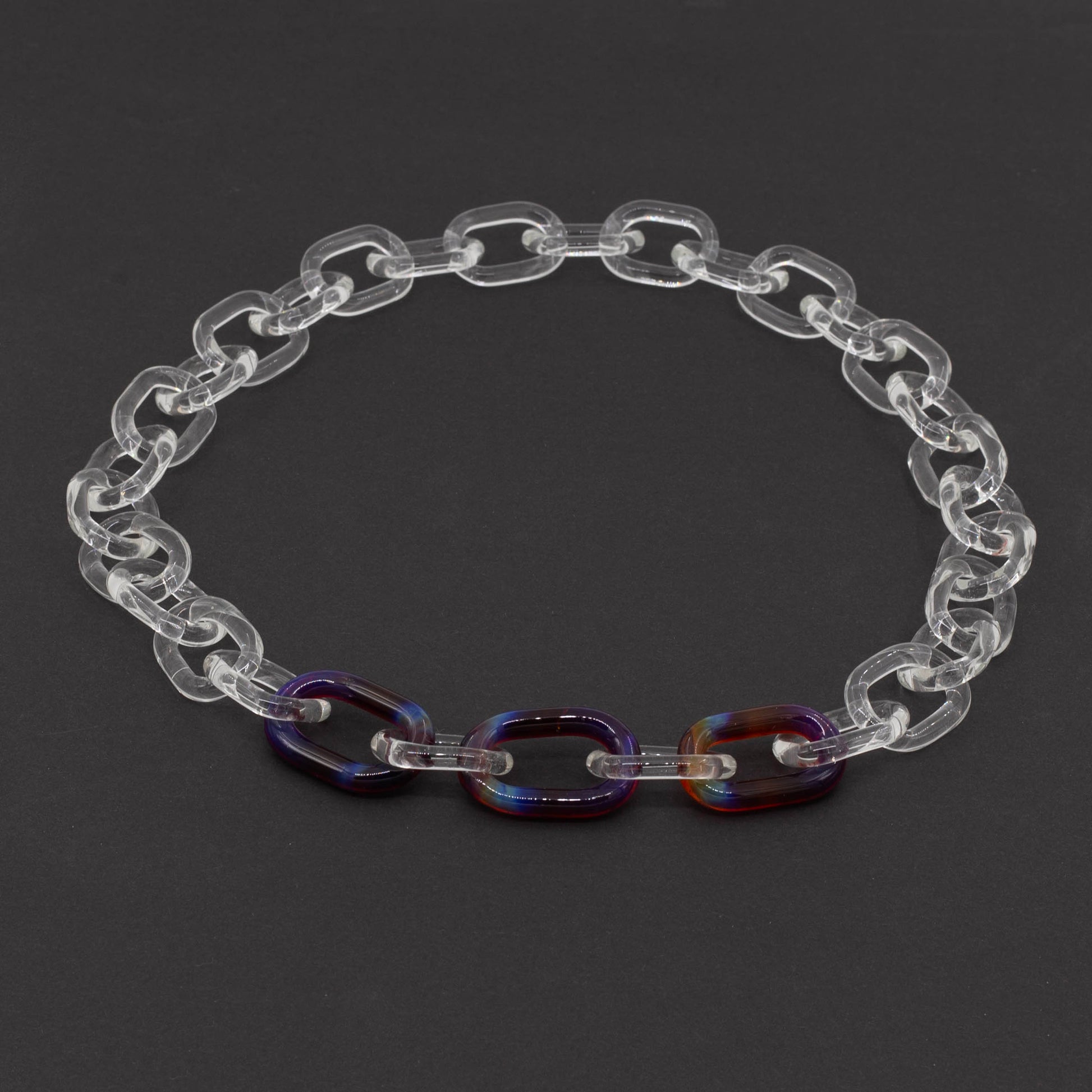 Dark background, necklace made from clear glass links with 3 coloured links