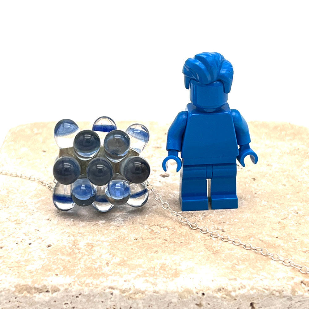 Glass bead with raised dots shown beside a blue Lego figure for scale. The bead comes to the elbow of the figure.