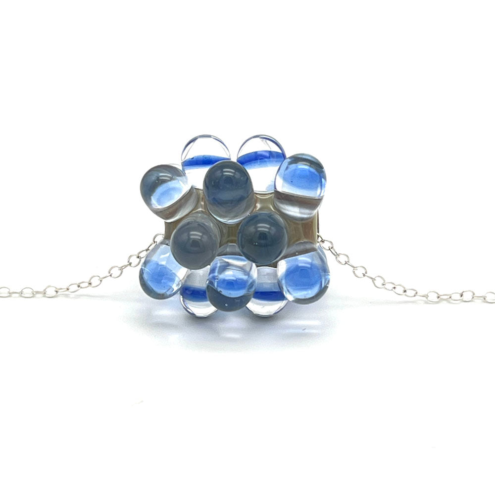 chunky bead glass bead with raised dots. The bead has a stone grey base with raised dots of clear and transparent blue glass. The bead sits on a sterling silver chain.