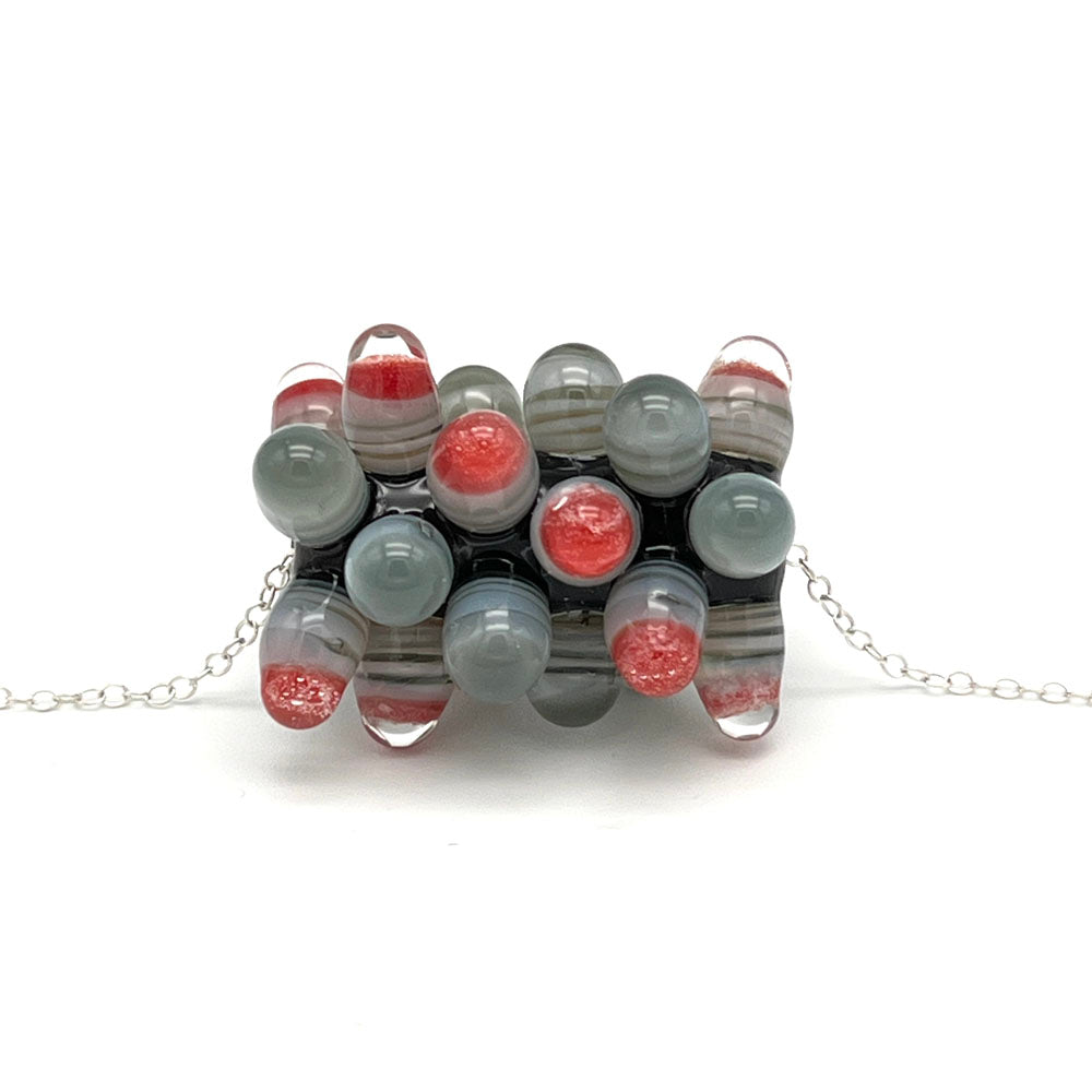 A tube shaped glass bead in dark glass decorated with raised dots. The bead sits on a fine sterling silver chain.