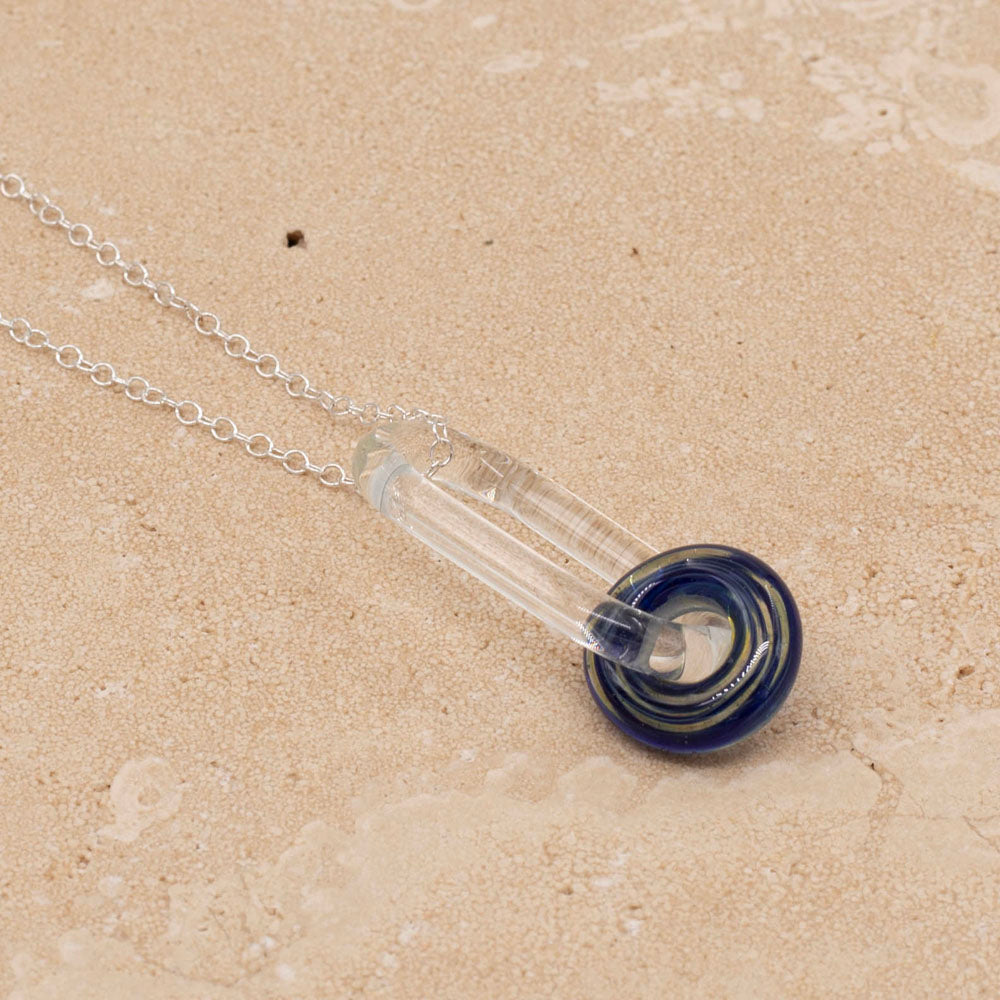 A necklace with sterling silver chain, clear glass link and blue green bead on a sandstone tile.